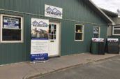 exterior of green building with roofing sample boards and tall hbm metal roofing and trim banner in front